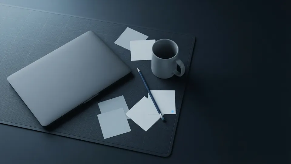 Loosely messy desk with a closed laptop, scattered blank sticky notes, a pencil and a plain grey mug